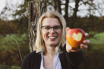 Frau hält Apfel in der Hand -Absolventen der Darmgesundheitscoach Ausbildung 
